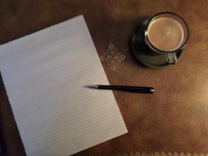 An overhead shot of a vintage writing desk, a pad, a pen and a cup of coffee.
