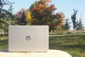 A laptop sitting on a rock in a park, in front of beautiful fall foliage. 