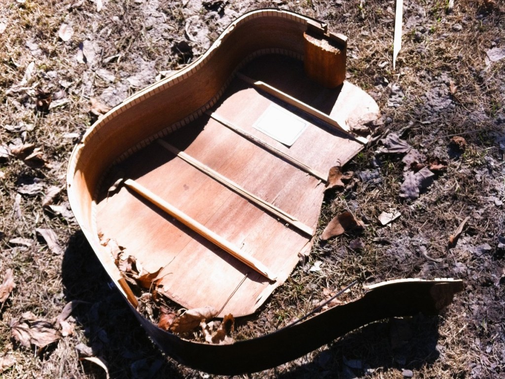 A broken guitar seen by the side of the road