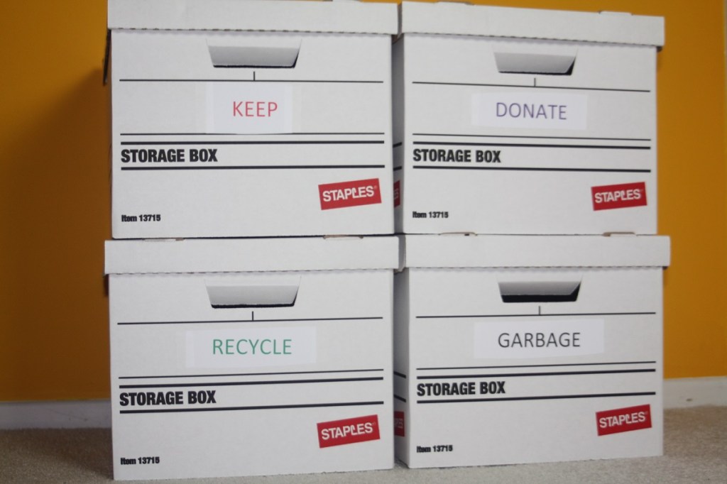 four banker's boxes intended to sort belongings. Their labels say keep, donate, recycle and garbage