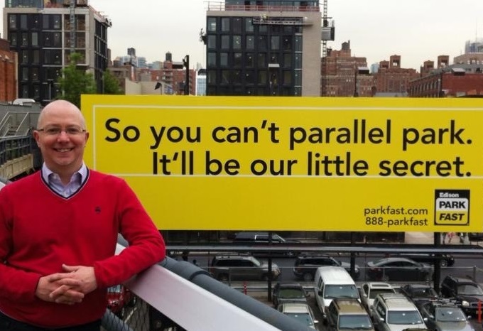 Me in front of a sign saying "So you can't parallel park, it'll be our little secret"