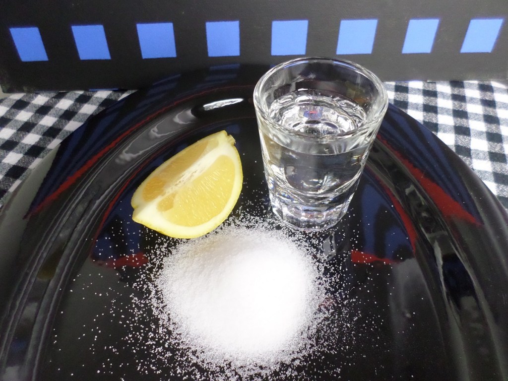 A plate with a lemon, a neat pile of salt and a glass containing an unspecified clear beverage.