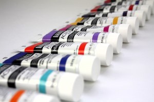 A selection of artists' acrylic paints, lined up diagonally on a white background.