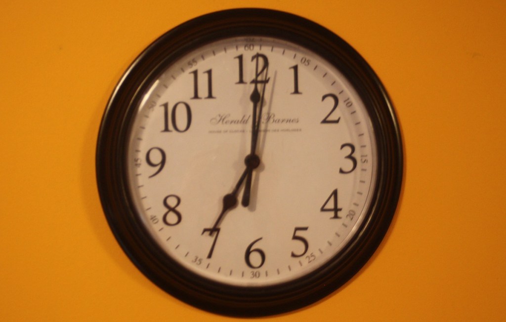 A clock on a yellow wall indicating 7 o'clock
