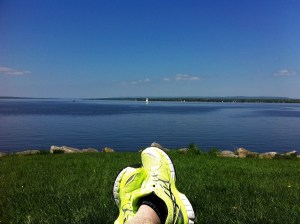 a panoramic shot of a sailboat on a calm river, with a pair of feet at the bottom of the shot enjoying the view