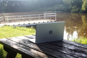 A laptop on a picnic table. In the background is a dock by the water.