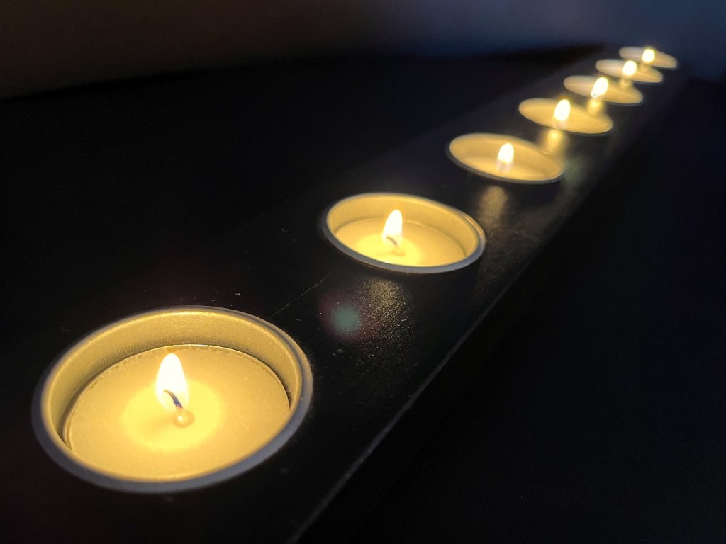 A row of seven tea lights flickering in the dark.