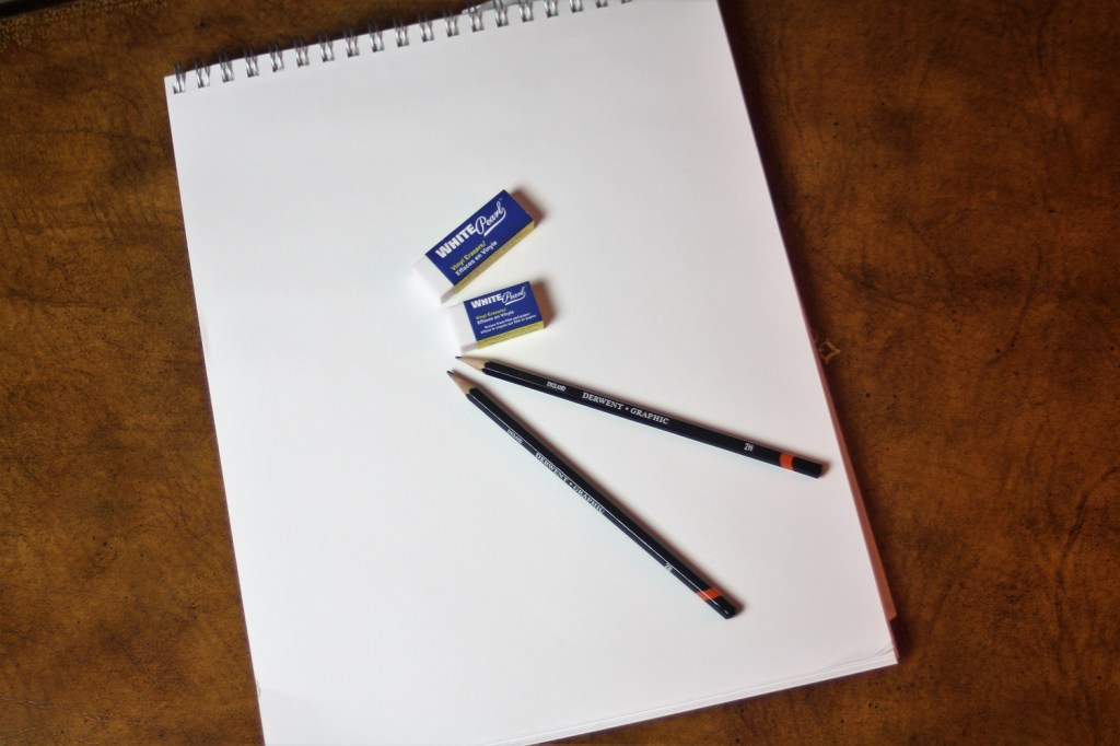 A sketch pad with two pencils and two erasers on a writing desk