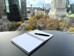 A pen sitting on an open journal on a black table with a panoramic view of downtown Montreal in the background.