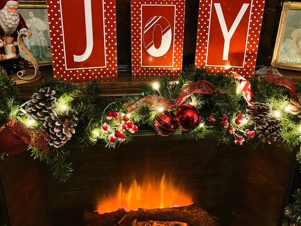 A fireplace decorated for Christmas with the letters spelling "joy" on the mantel.
