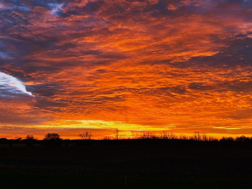 A striking shot of a rural sunset with the clouds illuminated in different shades of red and orange.