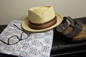 A hat, a pair of glasses, a floral short and a pair of Birkenstocks on a bench.