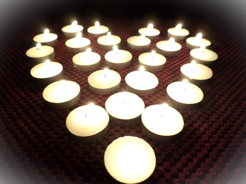 A collection of lit tea lights, arranged in the shape of a heart