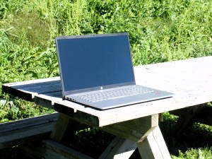 A notebook computer on a picnic table on a summer day.