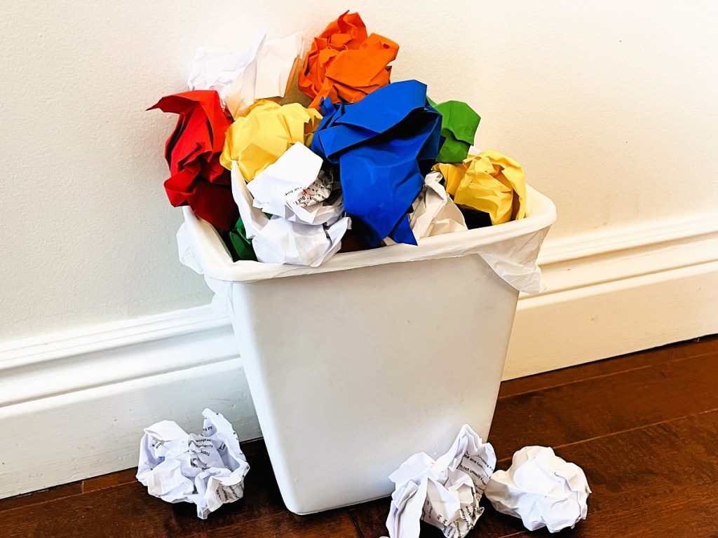 A garbage can containing colourful balls of paper, illustrating drafts gone wrong
