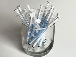 A glass containing oral syringes for giving medication to a cat.