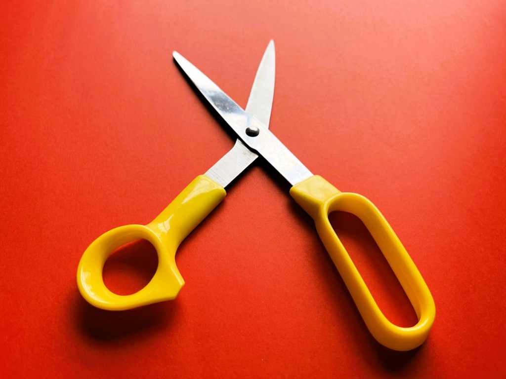 A pair of scissors with yellow handles on a red background.